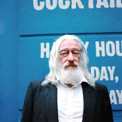 Man with a white beard against a blue Cocktails wall